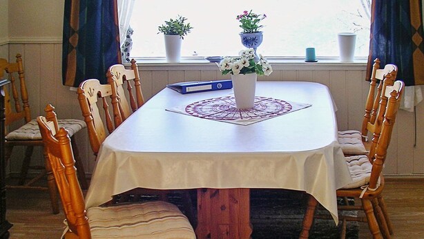 A dining table with a white tablecloth, surrounded by wooden chairs with cushioned seats. - 8 Person Holiday Home in Afarnes (Rauma)