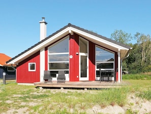 Ein rotes Haus mit einem großen Glasfenster, einem Schornstein und einer Terrasse mit Stühlen.