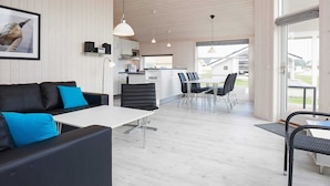 A modern interior with a sofa, dining table, and chairs. A kitchen area is visible with cabinets and a microwave. - Holiday Home in Großenbrode (Grossenbrode)
