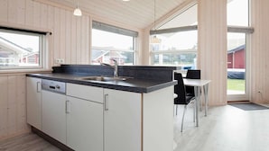 A modern kitchen with a central island, a sink, and a dining area with a table and chairs. - Holiday Home in Großenbrode (Grossenbrode)