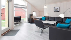 A modern living room with a sofa, a dining table, and a TV. - Holiday Home in Großenbrode (Grossenbrode)