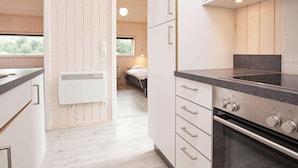 A modern kitchen with white cabinetry, a black countertop, and a built-in oven. There is a window providing natural light and a view of the outdoors. - Holiday Home in Großenbrode (Grossenbrode)