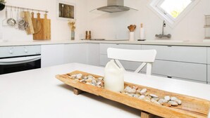 Una cocina moderna con armarios blancos, una tabla de cortar de madera con piedras, una silla blanca y una ventana con luz natural.