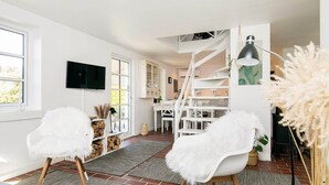 Una sala de estar moderna con muebles blancos, una escalera y un televisor montado en la pared.