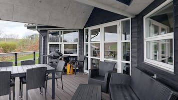 An outdoor deck with a grill, seating area, and large windows.