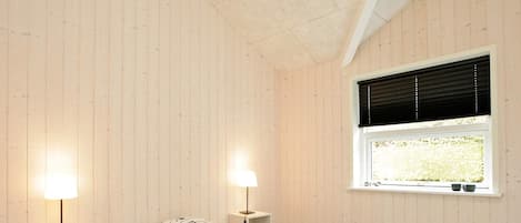 A bedroom with a bed, two bedside tables, a window with blinds, and a ceiling with exposed beams.
