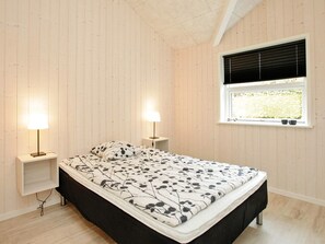 A bedroom with a bed, two bedside tables, a window with blinds, and a ceiling with exposed beams. - 4 Star Holiday Home in Roslev (Roslev)