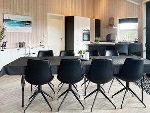A modern dining area with a long table and black chairs, a kitchen area with a stove and oven, and a painting on the wall. - 4 Star Holiday Home in Roslev (Roslev)