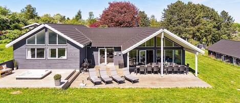 A modern house with a large deck, a hot tub, and a covered patio area.