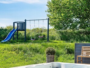 A playground with a slide and swings, surrounded by lush greenery and a wooden bench. - 5 Star Holiday Home in Vejby (Vejby)