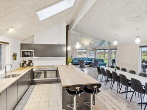 A modern kitchen with a central island, built-in appliances, and a dining area with a long table and chairs.