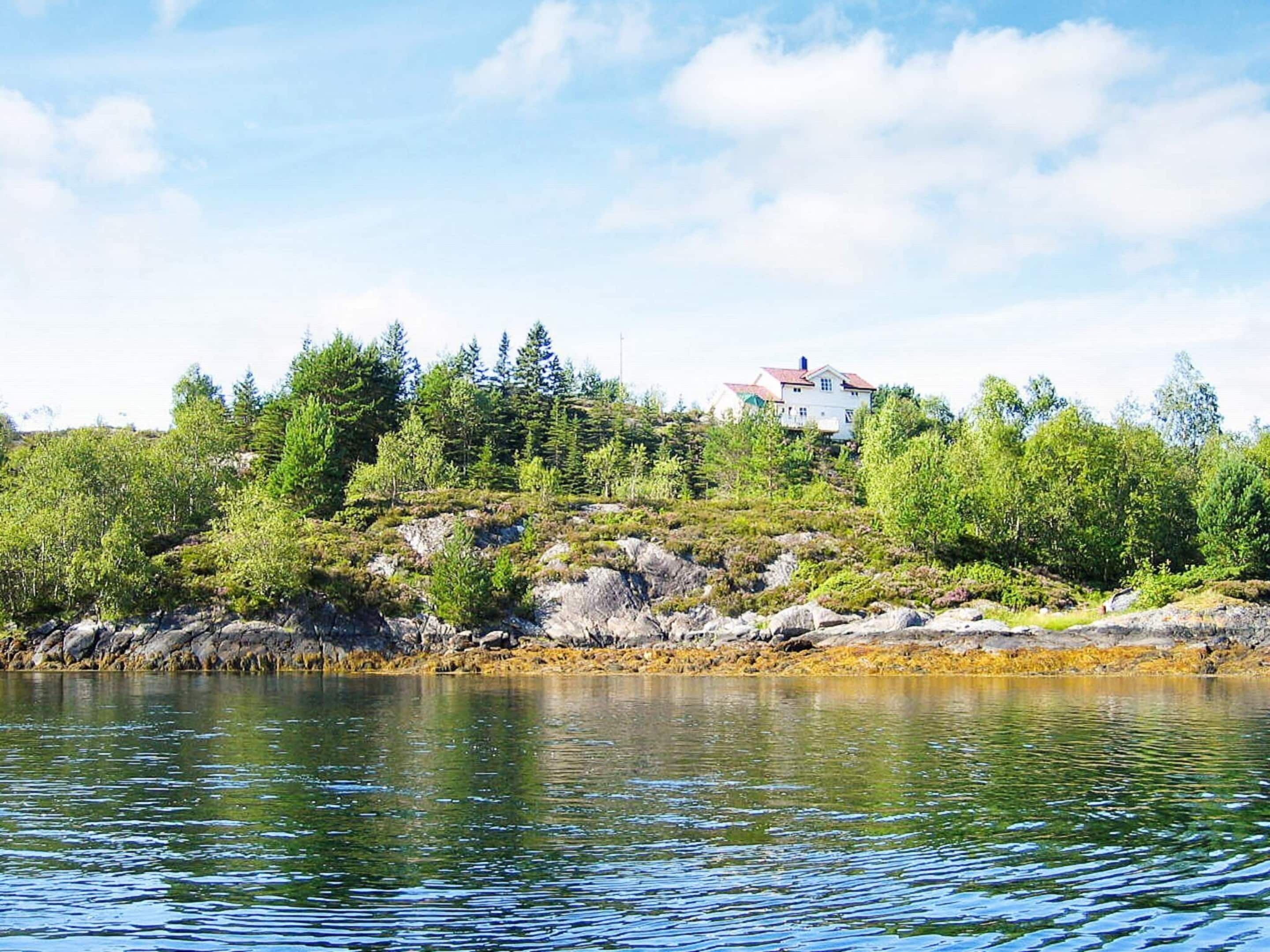A lakeside property with a house on a rocky hill, surrounded by dense greenery.
