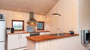 A modern kitchen with wooden walls, a central island with a sink, a stove, and a microwave. - 6 Person Holiday Home in Tarm-by Traum (Tarm)