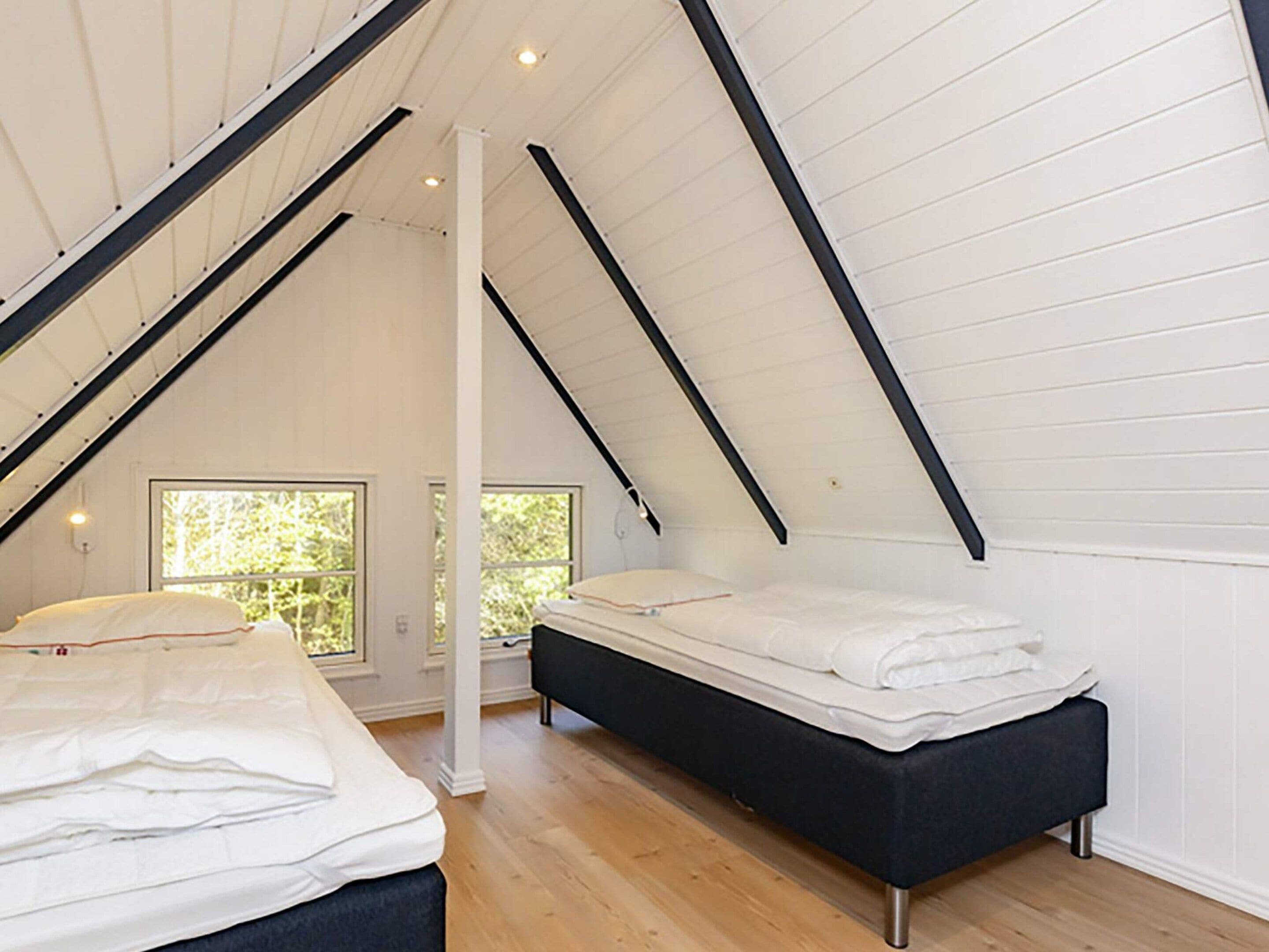 A bedroom with two beds, wooden flooring, white walls, and a sloped ceiling.