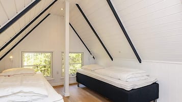 A bedroom with two beds, wooden flooring, white walls, and a sloped ceiling.