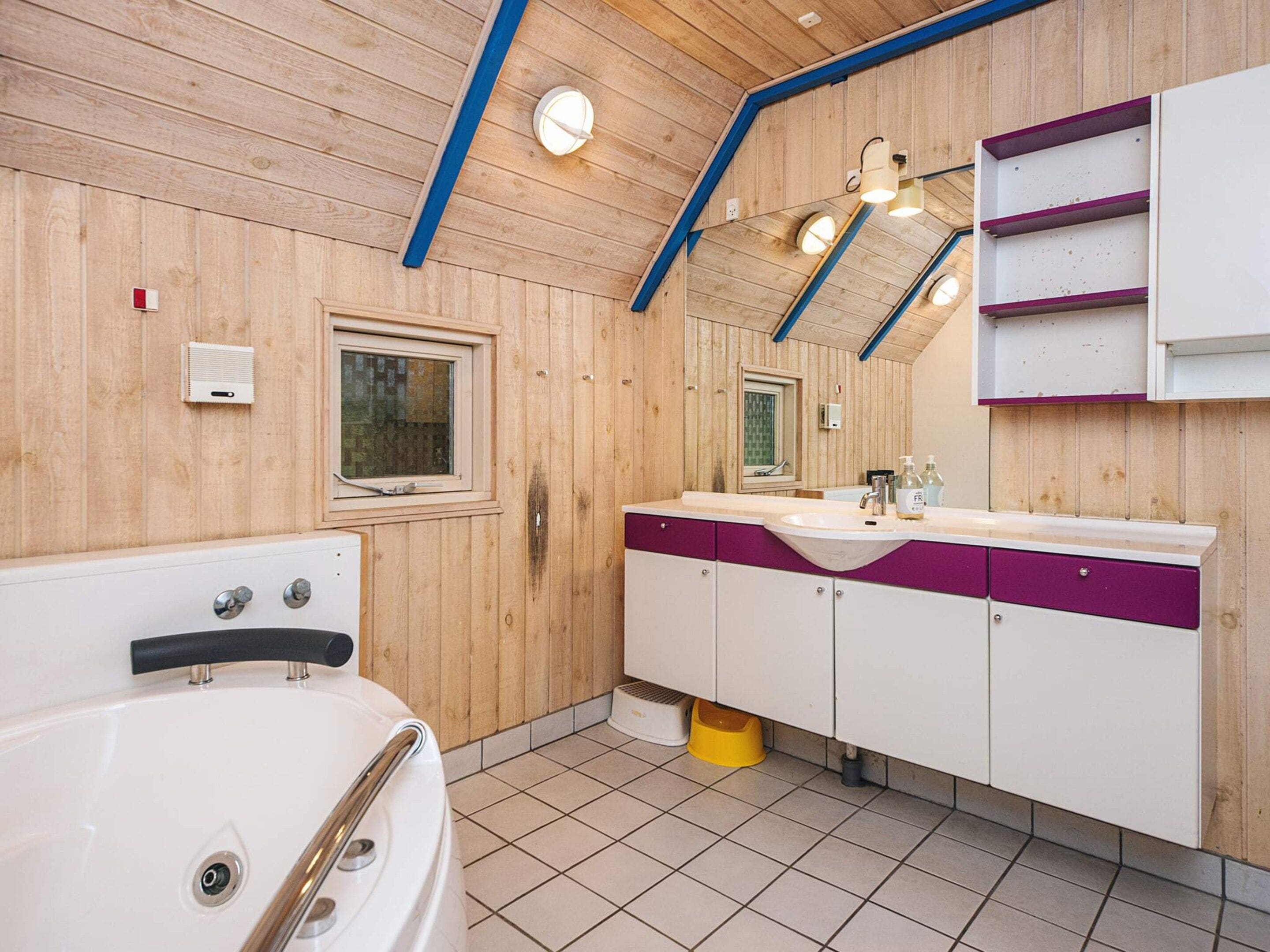 A bathroom with a wooden ceiling, a bathtub, a sink with a mirror, and a window.