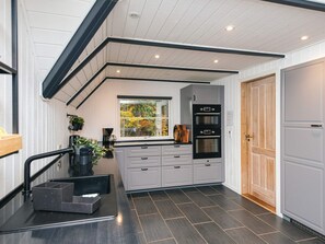 A modern kitchen with a built-in oven, a window with a view of trees, and a wooden door.
