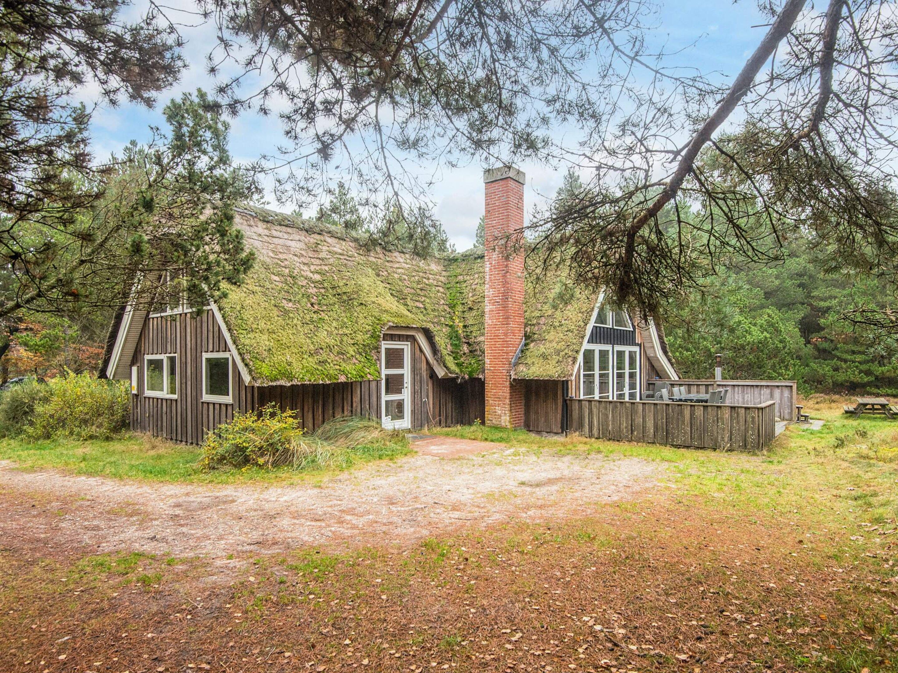 A rustic cabin with a thatched roof, a chimney, and a wooden fence.