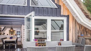 A modern house with a large glass door leading to a dining area with wicker furniture and a kitchen visible through the glass. - 10 Person Holiday Home in Blavand (Blavand)