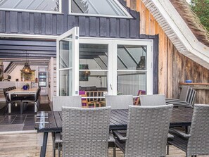A modern house with a large glass door leading to a dining area with wicker furniture and a kitchen visible through the glass. - 10 Person Holiday Home in Blavand (Blavand)