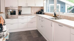 A modern kitchen with white cabinets, stainless steel appliances, and a window overlooking a residential area. - 4 Star Holiday Home in Glesborg (Glesborg)