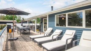 A covered outdoor deck with lounge chairs, a grill, and a dining area. - 4 Star Holiday Home in Glesborg (Glesborg)