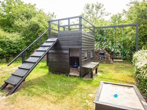A wooden playhouse with a ramp and a swing set in a garden. - 4 Star Holiday Home in Glesborg (Glesborg)