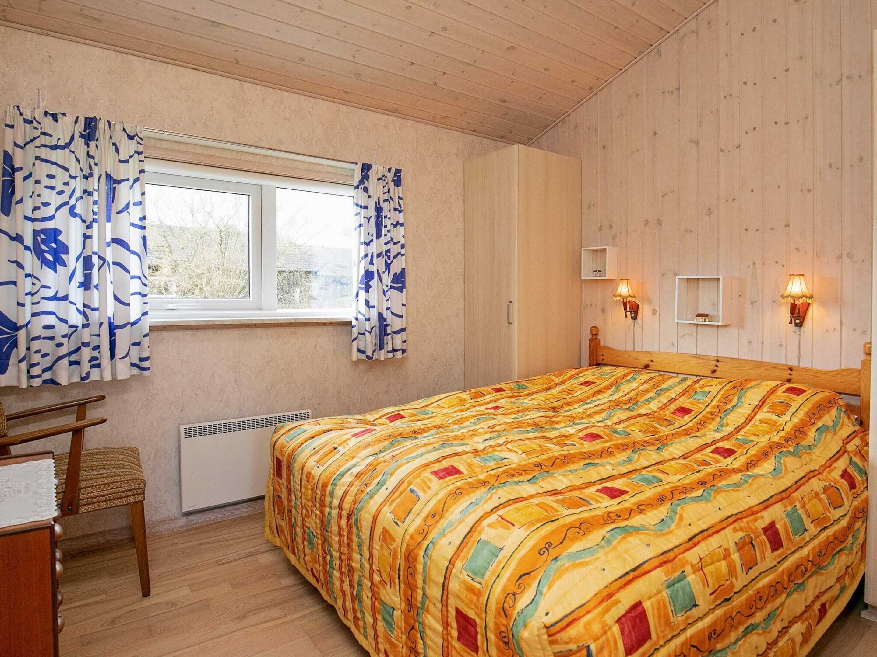 A bedroom with a wooden bed, a window with curtains, a radiator, a chair, and wall-mounted lamps.