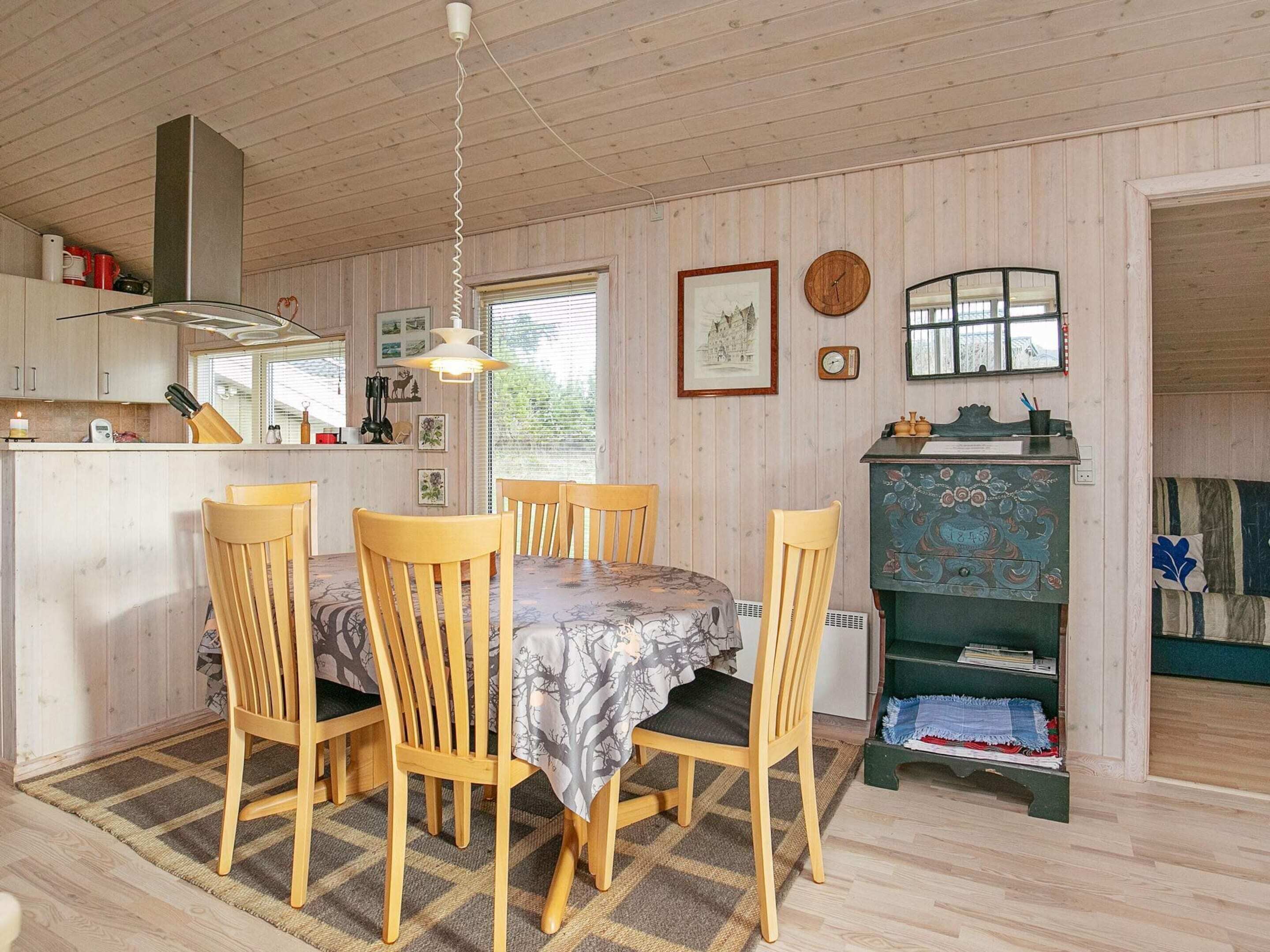 Une pièce chaleureuse aux murs lambrissés, avec une table à manger pour quatre personnes, un coin cuisine et une bibliothèque.