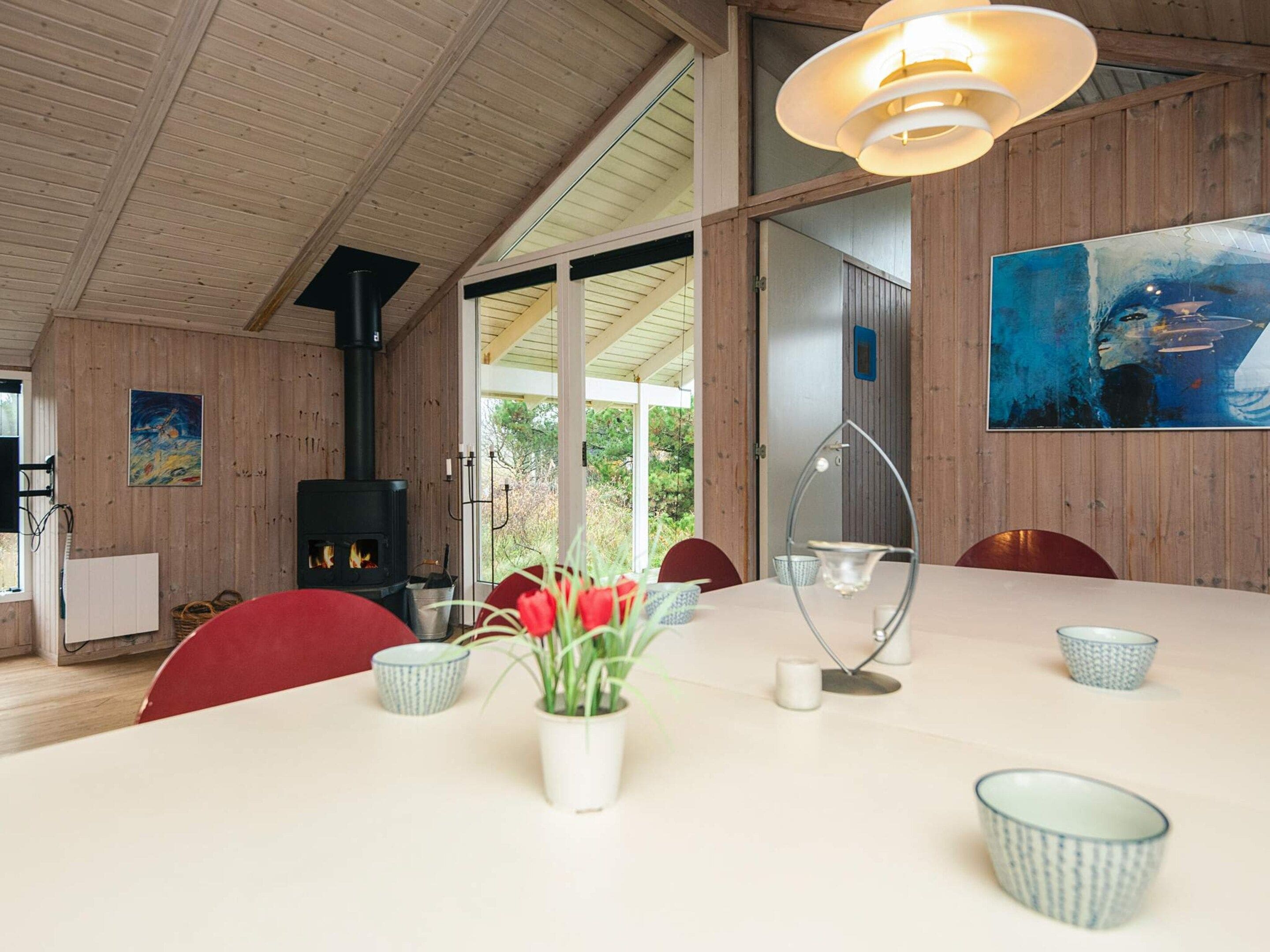 A dining area with a large table, chairs, a vase with flowers, and a painting on the wall.