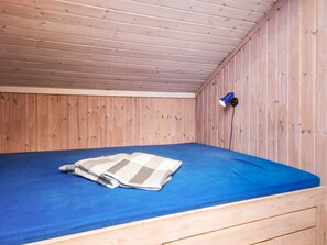 A small, single-bed room with a wooden ceiling and walls, a blue mattress, and a blue lamp on the wall. - Serene Holiday Home in Oksbøl near Beach (Oksbol)
