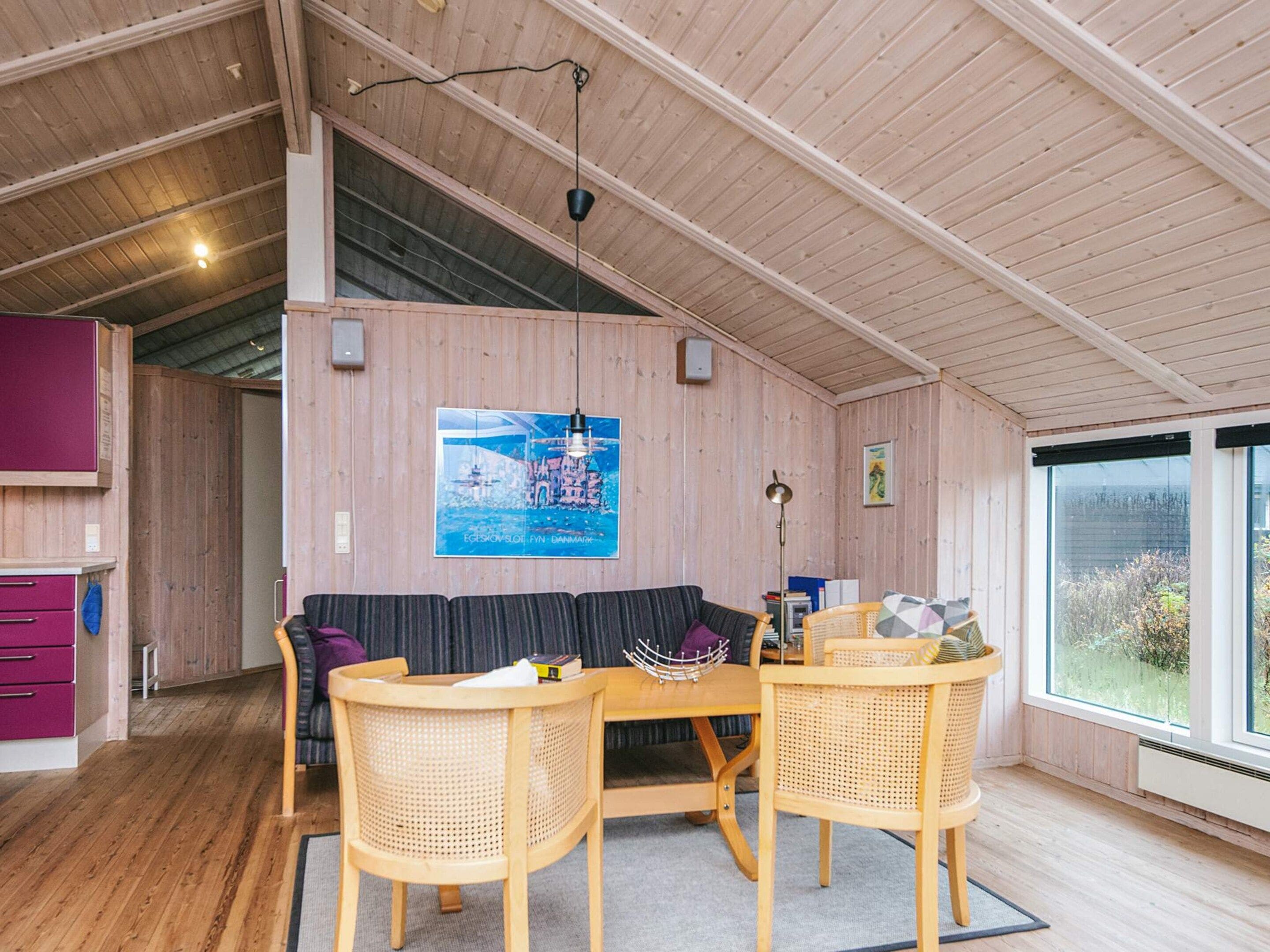 A cozy room with a wooden ceiling, a sofa, two chairs, a table, and a poster on the wall.