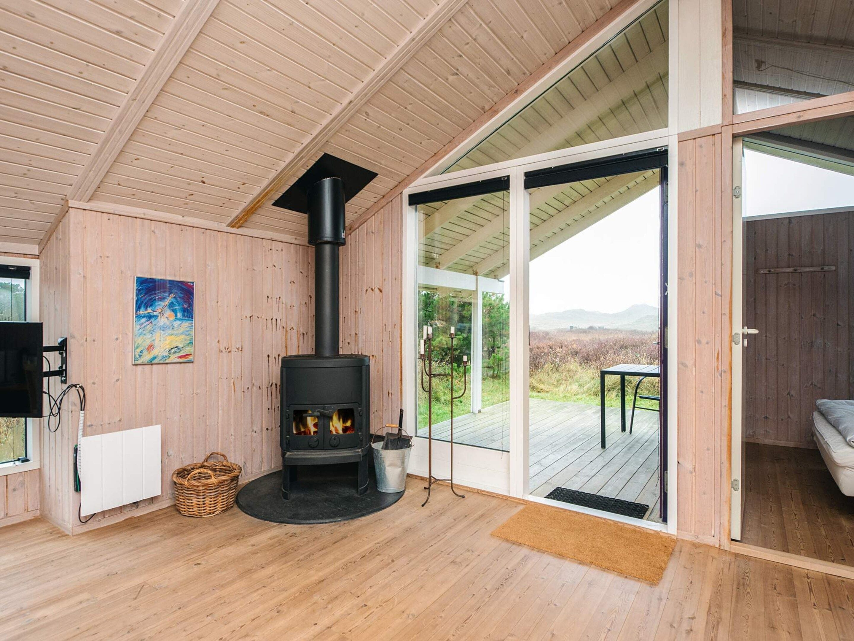 Habitació amb una estufa de llenya, un gran finestral de vidre que dona a una terrassa exterior i un quadre a la paret.