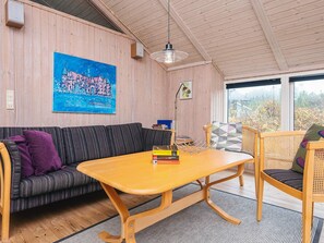 A cozy room with a wooden ceiling, a sofa, a table, and a chair. There's a painting on the wall and a window with a view. - Serene Holiday Home in Oksbøl near Beach (Oksbol)