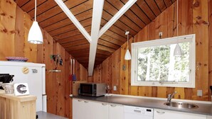 A compact kitchen with wooden walls, a microwave, a sink, and a window with a view of trees.