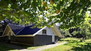 A small, single-story building with a blue roof, surrounded by grass and trees.