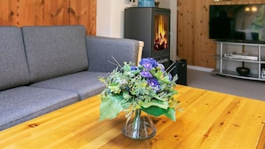 A cozy living room with a grey sofa, a wooden table with a vase of flowers, a fireplace, and a television.