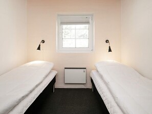 A small, single-room accommodation with two single beds, a window with blinds, a wall-mounted heater, and two wall lamps. - 12 Person Holiday Home in Ulfborg (Ulfborg)