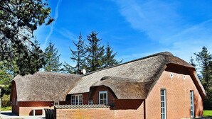 A traditional brick building with a thatched roof, surrounded by a grassy area and trees. - 12 Person Holiday Home in Ulfborg (Ulfborg)