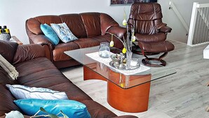 A brown leather sofa with blue cushions, a glass coffee table with decorative items, and a brown leather armchair. - Holiday Home in BrattvÃ¥g (Ålesund)
