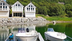 A waterfront property with three white houses, a dock with two boats, and a forested hillside in the background. - Holiday Home in BrattvÃ¥g (Ålesund)