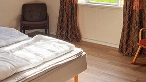 Ein Schlafzimmer mit einem Bett, Holzboden, einem Sessel und Vorhängen.