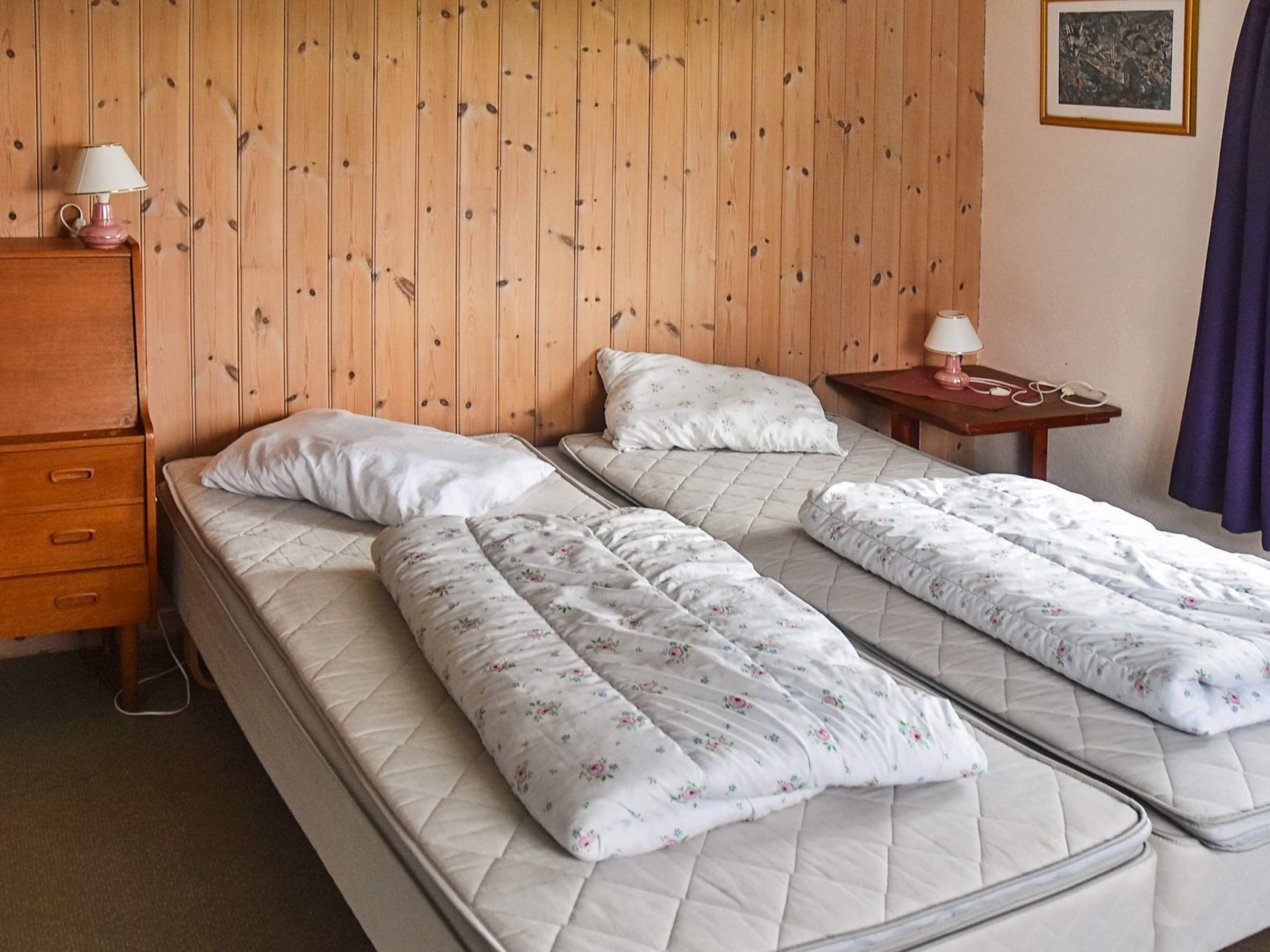 A room with two beds, a wooden headboard, a nightstand with a lamp, and a dresser.