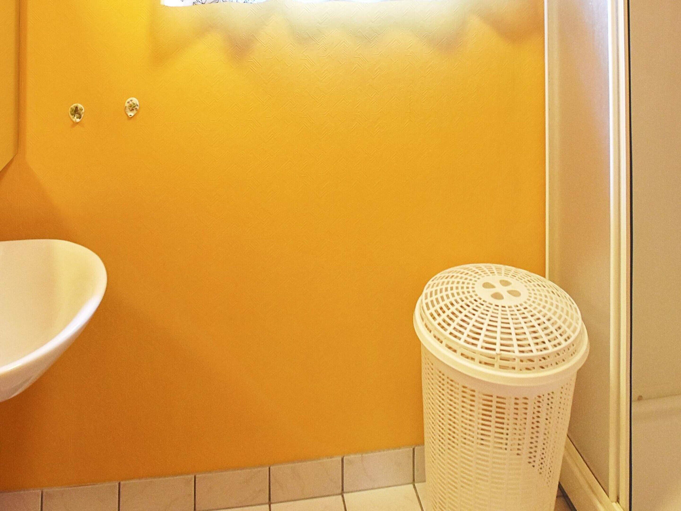 A bathroom with a white sink, a white laundry basket, and a yellow wall.