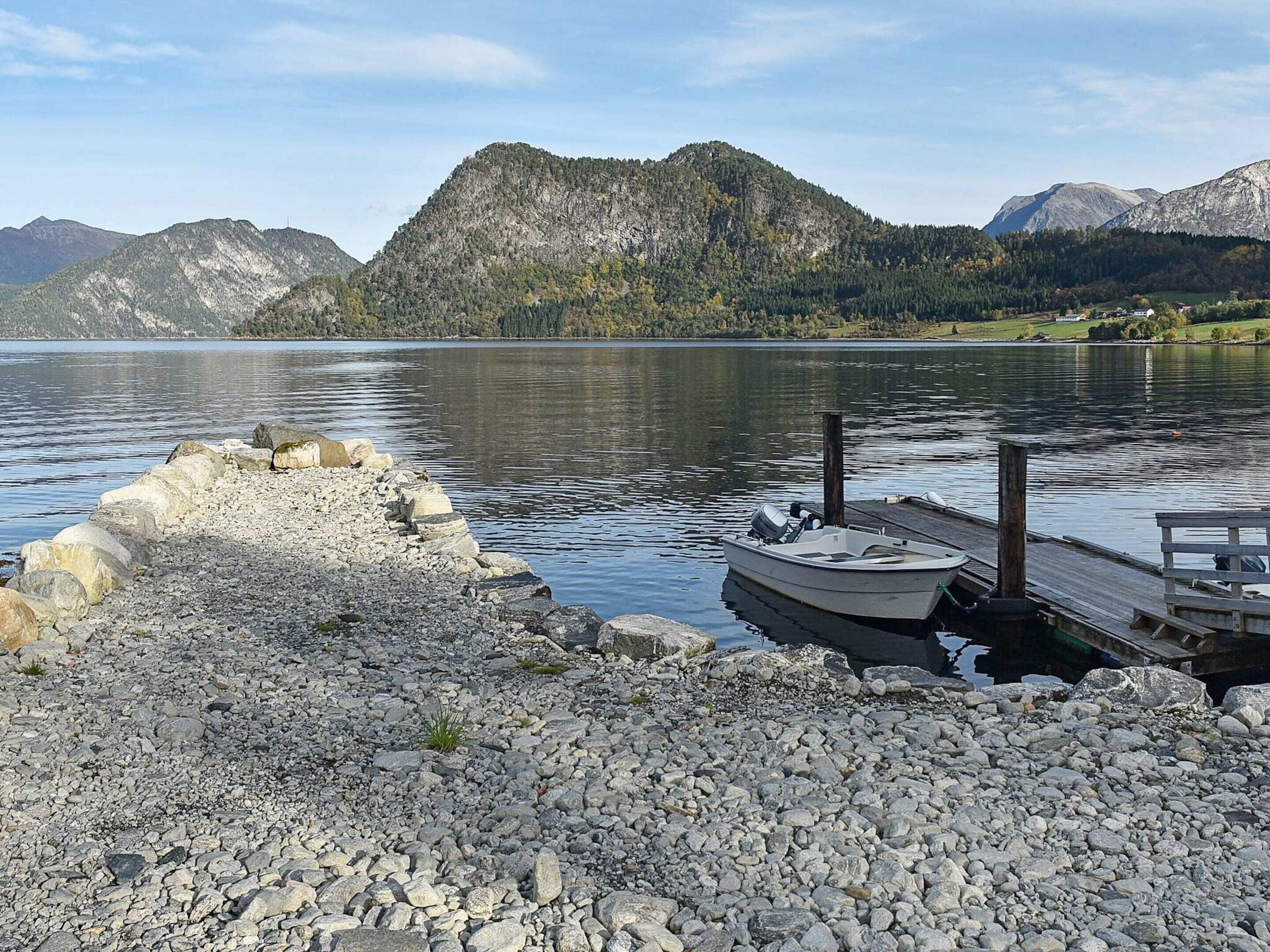 Une côte rocheuse avec un quai et un bateau, entourée de montagnes et bordée d’un lac paisible.