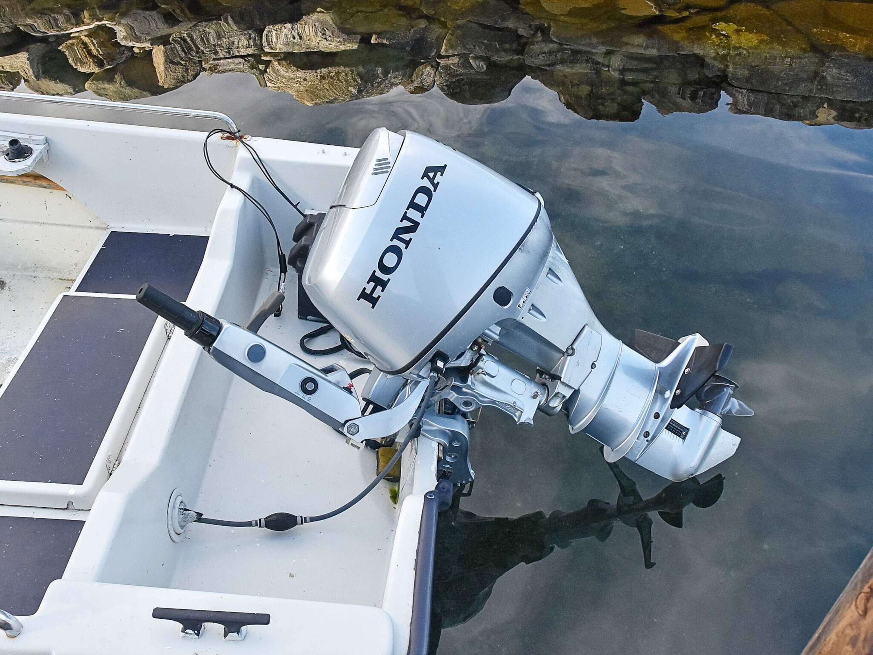 A boat with a Honda outboard motor, a white hull, and a stone wall in the background.
