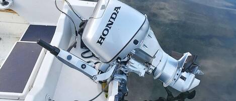 A boat with a Honda outboard motor, a white hull, and a stone wall in the background.