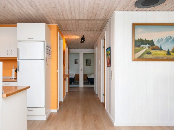 A hallway with a kitchen on the left, a bedroom with a bed and dresser, and a living area with a painting on the wall. - 8 Person Holiday Home in Ulfborg (Ulfborg)