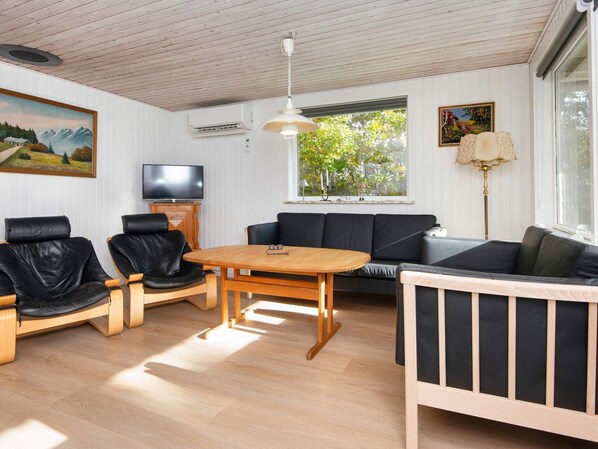 Ett vardagsrum med ett träbord, svarta läderstolar, en soffa och en tv.