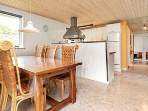 A dining area with a wooden table and chairs, a kitchen with white cabinets, and a visible clock on the wall.